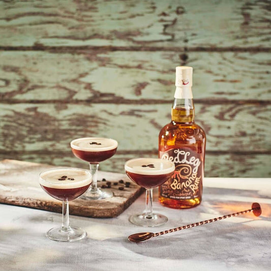 Bottle of RedLeg Banana Rum with 3 espresso martini glasses against wooden backdrop