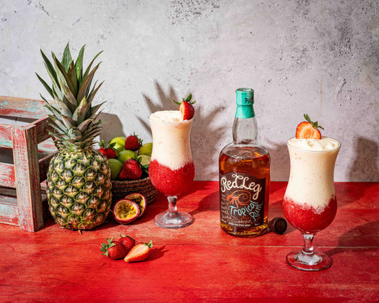 Bottle of RedLeg Tropical Rum, two Lava Flow cocktails with creamy coconut and strawberry swirls, garnished with fresh strawberries.