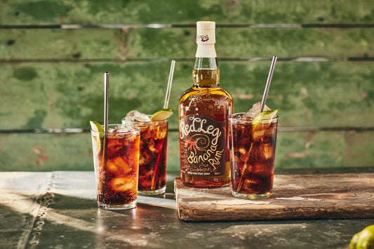 Bottle of RedLeg Banana Rum next to 3 tall glasses against a green wooden backdrop